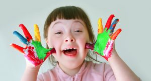 Vesela deklica z Downovim sindromom kaže dlani, pisani od barv. 
