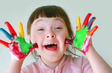 Vesela deklica z Downovim sindromom kaže dlani, pisani od barv.